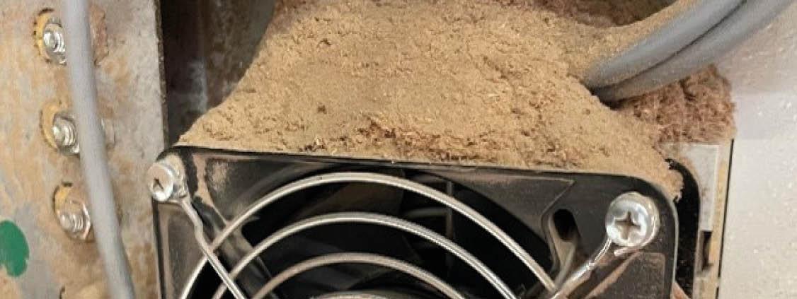 Close-up of an industrial cooling fan heavily covered with dust and debris.